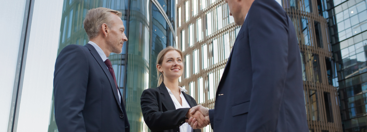 Three business people shaking hands in front of a building, symbolizing a successful partnership.
